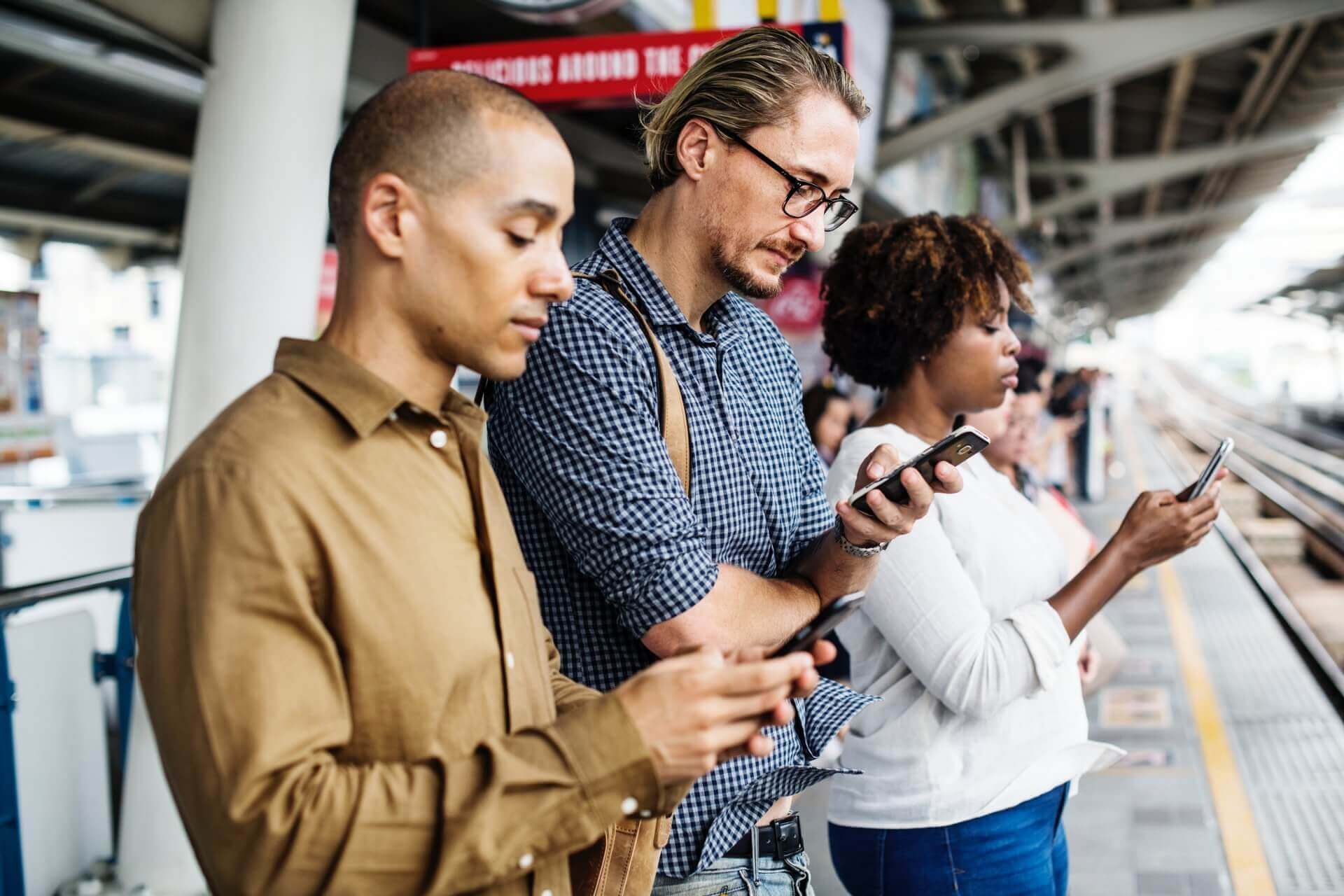 Big Data im E-Commerce wird über drei Personen visualisiert, die ein Smartphone am Gleis eines Bahnhofs nutzen.