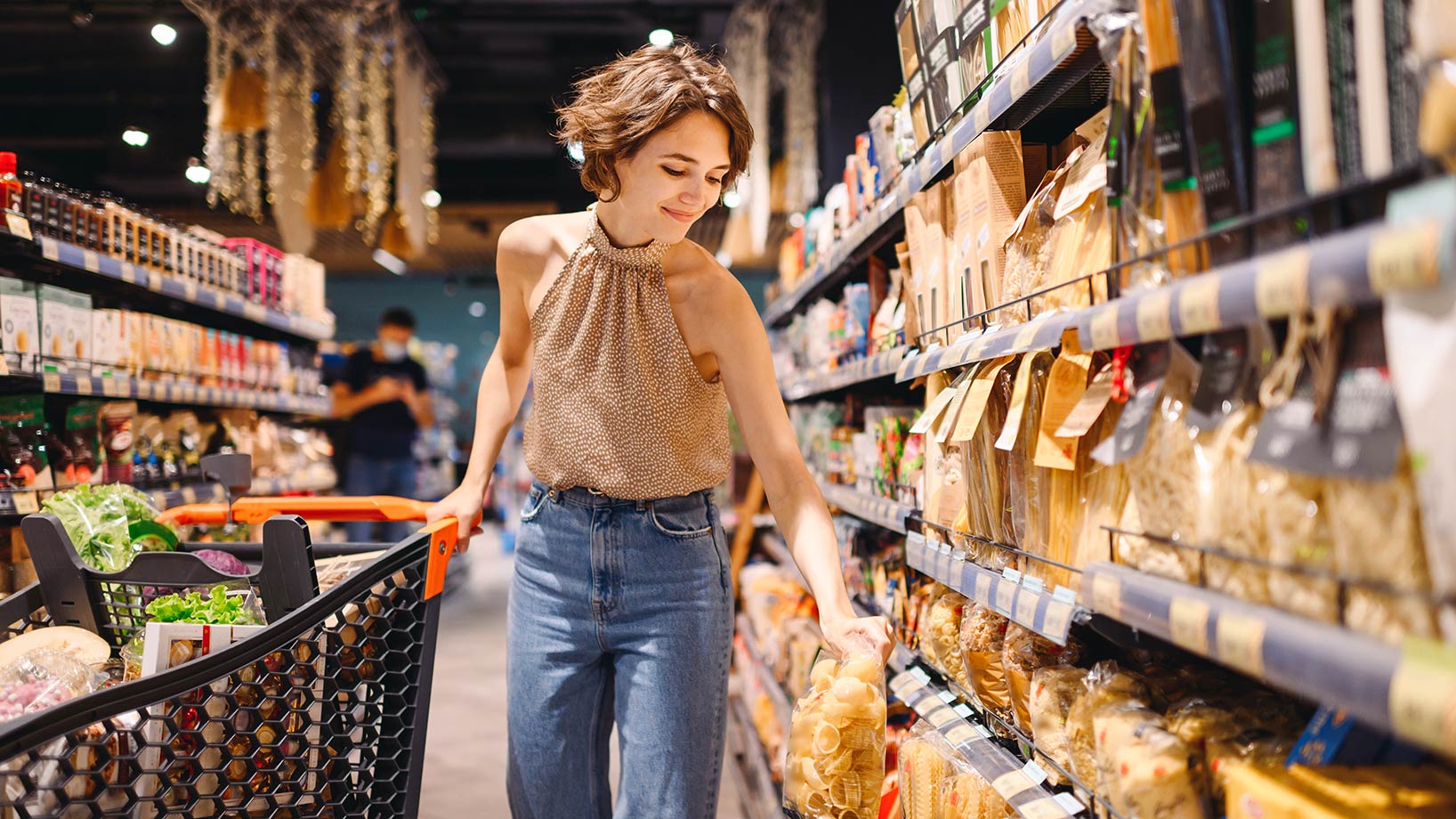 Eine Frau im Supermarkt steht zwischen zwei Regalen mit Pasta und Soßen, ein Beispiel für sinnvolles Category Management.