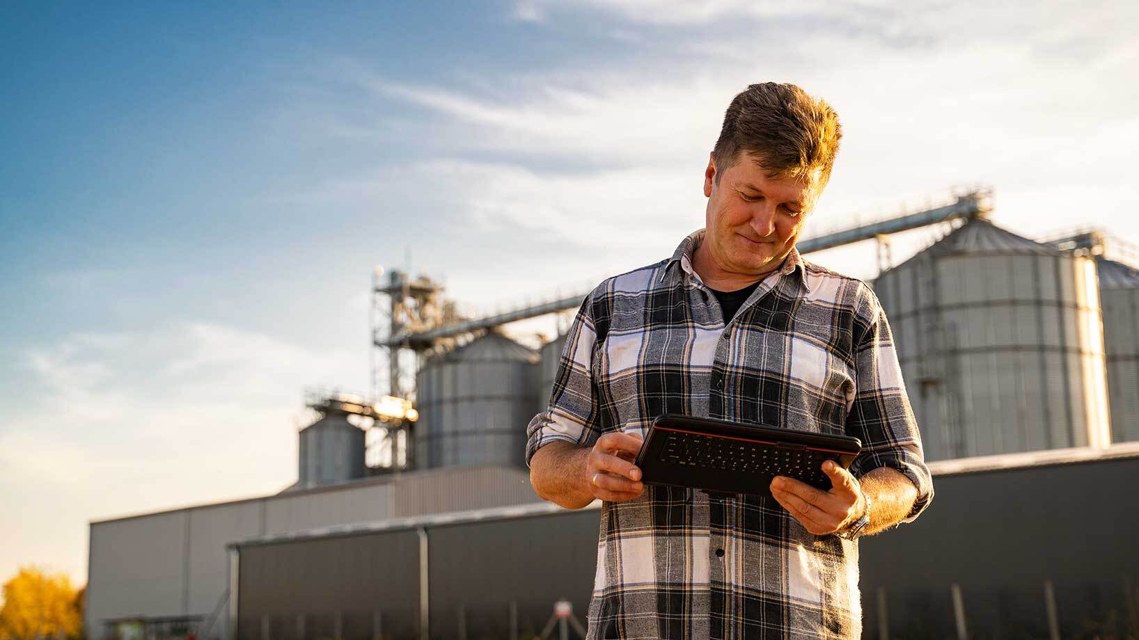 Auf dem Bild ist ein Mann mit einem Tablet zu sehen, der vor mehreren Silos steht.