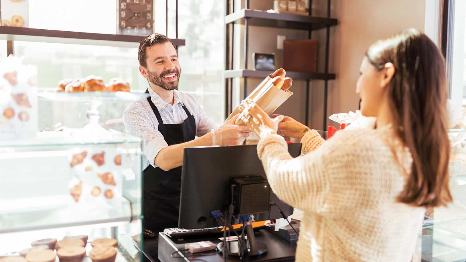 Eine Frau kauft bei einem Bäcker Baguettes.